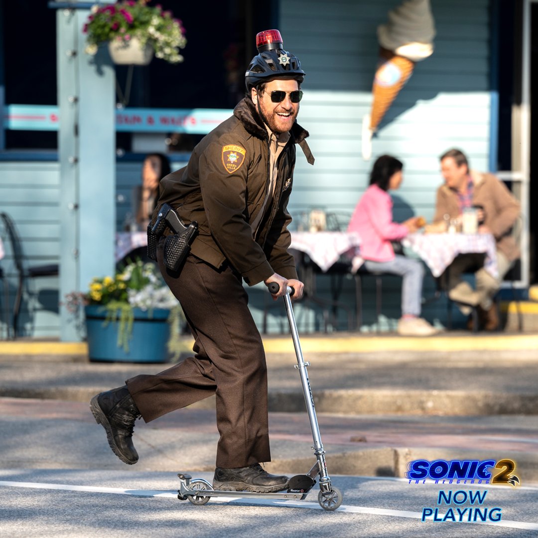 A picture of a man with brown facial hair who is riding a scooter with a little police hat siren on his head