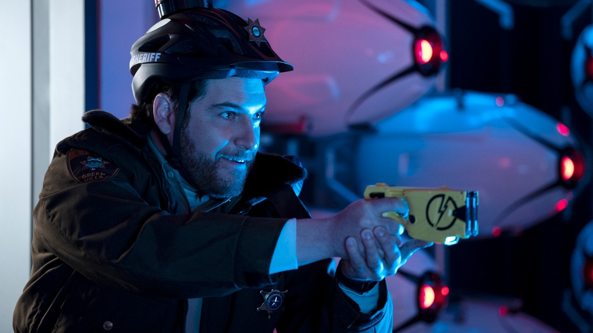 A picture of a man with brown facial hair holding a taser with a determined look on his face